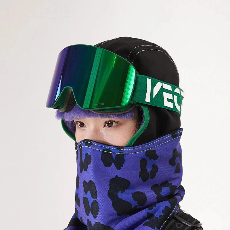 Rider wearing the Forest Green / Green Mirror cylindrical goggle, strap with white brand lettering, over a black balaclava with a purple leopard-print face cover