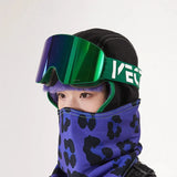 Rider wearing the Forest Green / Green Mirror cylindrical goggle, strap with white brand lettering, over a black balaclava with a purple leopard-print face cover