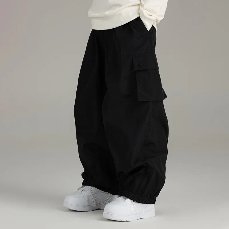 Sidehit Baggy Cargo Snow Pant in Black, side view on a grey background, showing the wide leg, snap-flap thigh cargo pocket and elasticated cuffs
