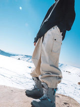 Sidehit Baggy Cargo Snow Pant in Khaki, worn on a snowy ridge, side view of the snap-flap thigh cargo pocket and elasticated cuffs